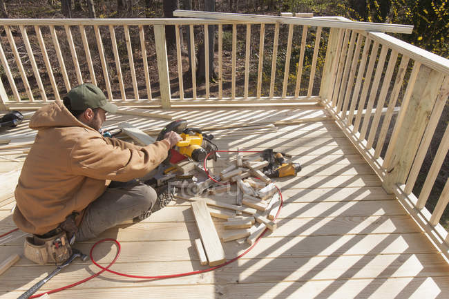 Carpinteiro hispânico usando serra de corte para cortar a tampa de corrimão deck — Fotografia de Stock