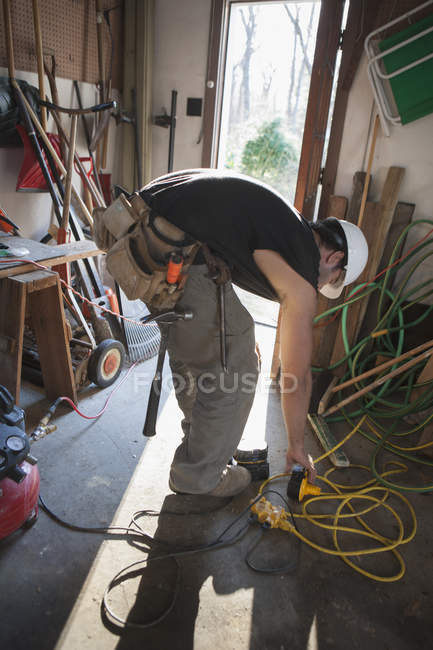 Hispanic carpenter plugging in rechargeable battery in home garage — Stock Photo