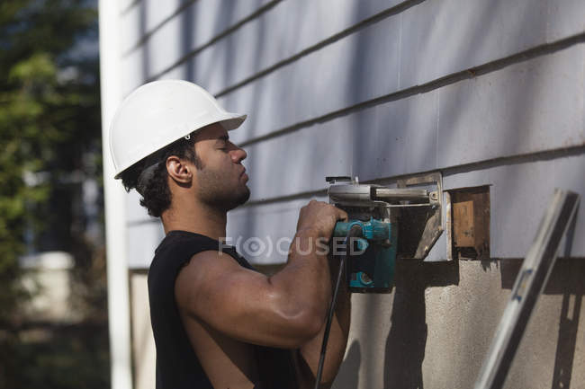 Hispanic carpenter trimming house siding for installation of new deck — Stock Photo