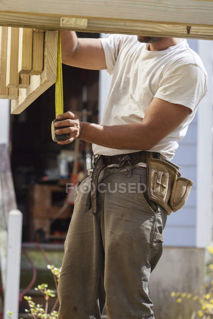 Hispanic carpenter measuring rim joist for deck construction — Stock Photo