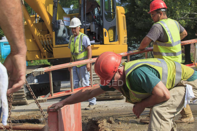 Bauarbeiter bereiten sich darauf vor, mit Leiter in Loch zu klettern — Stockfoto
