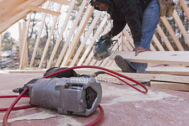 Carpenter cutting rafter using a circular saw with a nail gun on foreground — Stock Photo