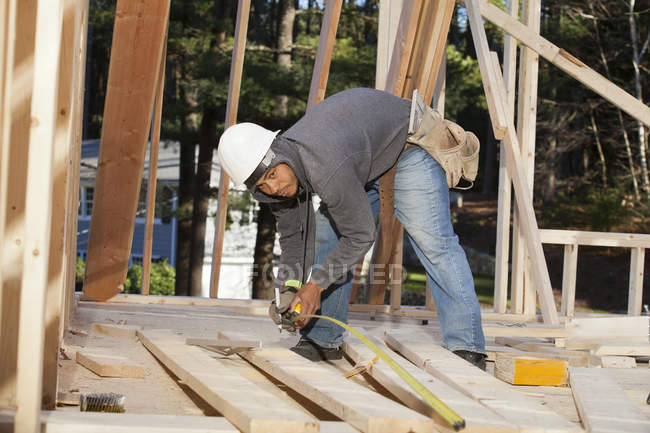 Carpenter measuring board length for house construction — Stock Photo
