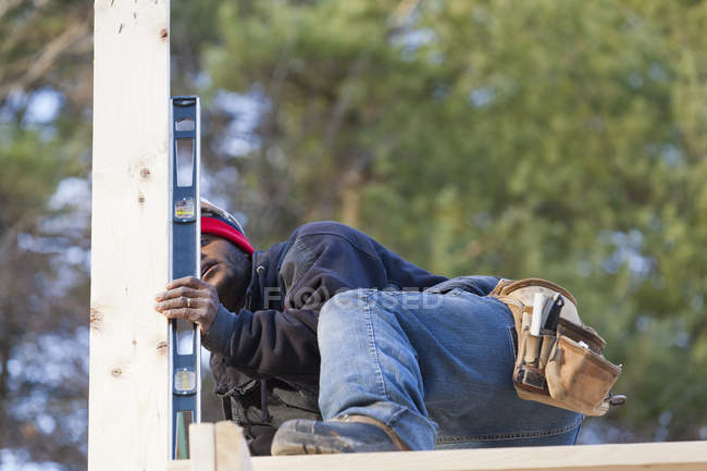 Carpinteiro usando um nível para medir o suporte vertical do telhado — Fotografia de Stock