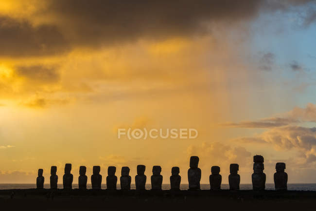 Los quince moais de Tongariki se silueta contra el cielo brillantemente coloreado de la salida del sol; Isla de Pascua, Chile - foto de stock
