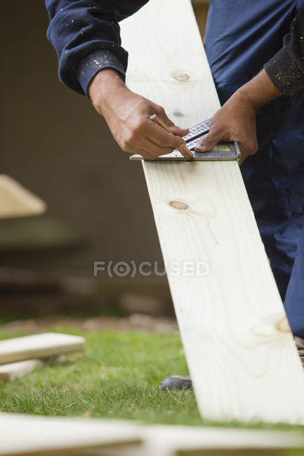 Carpintero usando cuadrado para marcar corte a bordo para la construcción - foto de stock