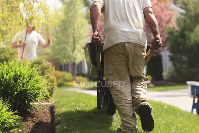 Paisajista llevando mantillo a un jardín en carretilla - foto de stock
