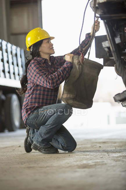 Female power engineer attaching canvas bucket to equipment truck — Stock Photo