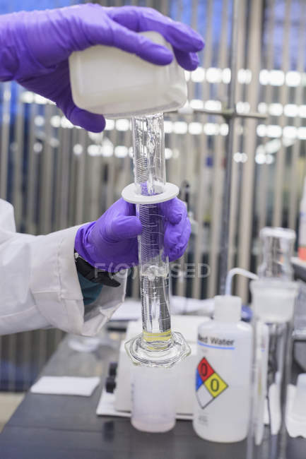 Tecnico di laboratorio che aggiunge liquido al cilindro graduato — Foto stock