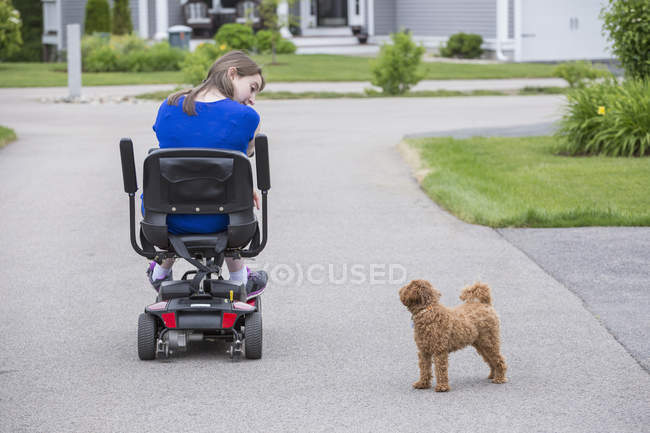 Молодая женщина с церебральным параличом играет со своей собакой, сидя на скутере — стоковое фото