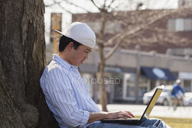 Estudante chinês sentado sob uma árvore usando laptop — Fotografia de Stock
