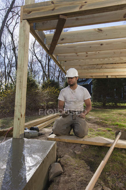 Hispanic carpenter with trowel inspecting deck footing — Stock Photo