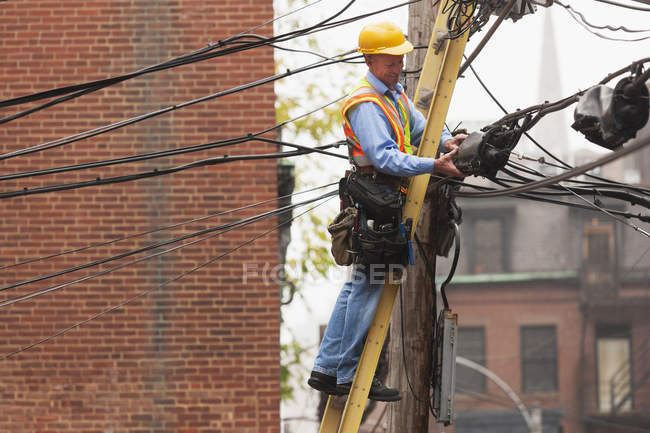 Cable lineman assessing a weather proofing boot for suspended wire connections in the city — Stock Photo