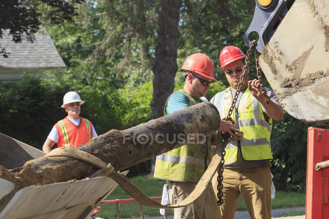 Construction workers unhooking old watermain from excavator — Stock Photo