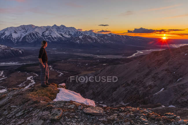 Un randonneur observant le coucher du soleil depuis une crête montagneuse dans la chaîne de l'Alaska ; Alaska, États-Unis d'Amérique — Photo de stock