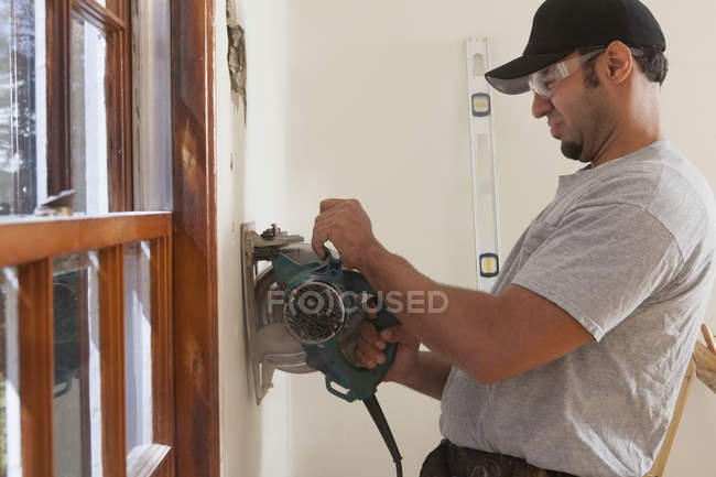 Carpintero hispano usando sierra circular para cortar el tablero de pared para la puerta de la cubierta en casa - foto de stock