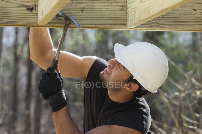 Hispanic carpenter nailing pressure treated deck joist with hammer — Stock Photo