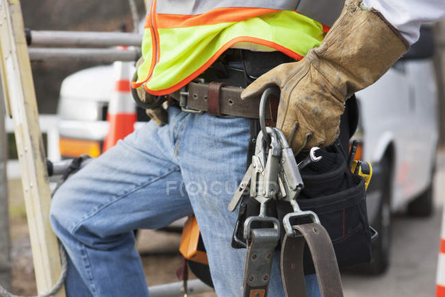 Trabajador de línea eléctrica con cinturón de herramientas y arnés de seguridad en su camión - foto de stock