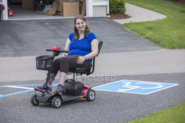 Jeune femme atteinte de paralysie cérébrale dans son scooter avec stationnement pour personnes handicapées — Photo de stock