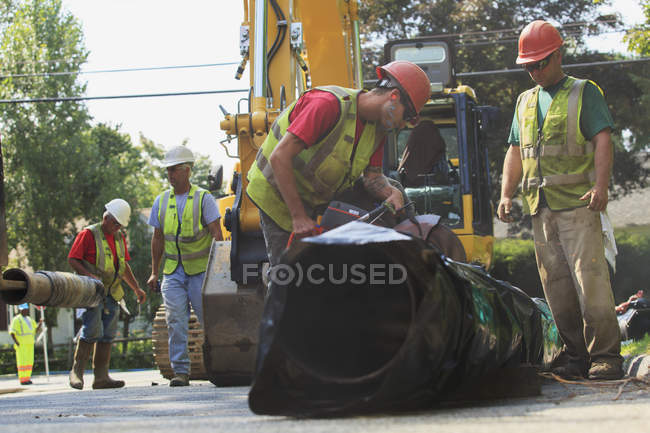 Construction workers cutting water main to length with gas powered saw — Stock Photo