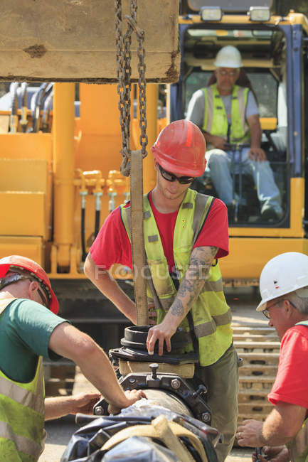 Travailleurs de la construction attachant des sections de conduite d'eau ensemble devant la pelle — Photo de stock