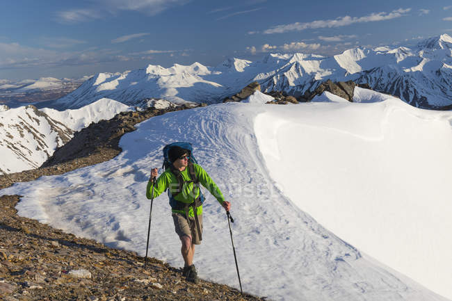 A hiker traverses a snowy ridge in the Alaska Range in early summer; Alaska, United States of America — Stock Photo