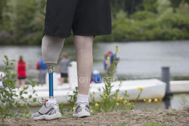 Homme avec une jambe prothétique debout sur le quai et regardant la course de bateau — Photo de stock
