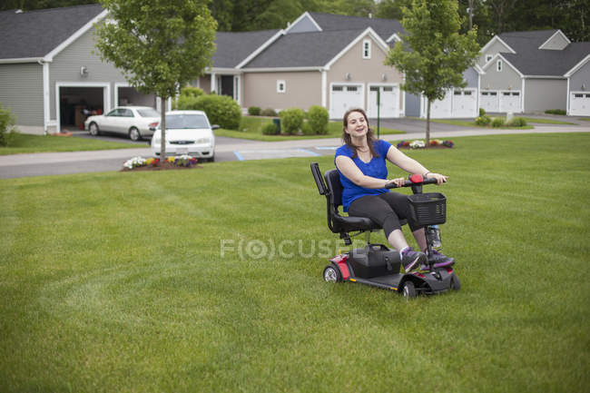 Mujer joven con parálisis cerebral montando su scooter en su césped - foto de stock