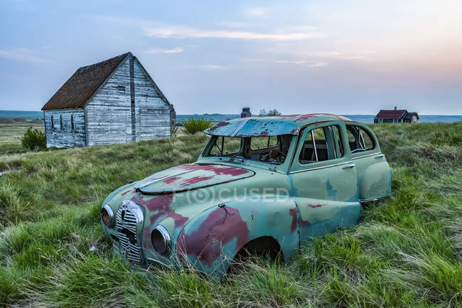 Винтажный автомобиль в заросшем травой поле со старыми постройками на ферме; — стоковое фото