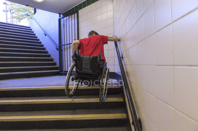 Модний чоловік з травмою спинного мозку в інвалідному візку, що йде по сходах метро назад — стокове фото