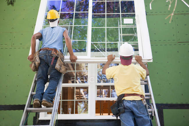 Zimmerleute positionieren einen großen Fensterrahmen an einem im Bau befindlichen Haus — Stockfoto