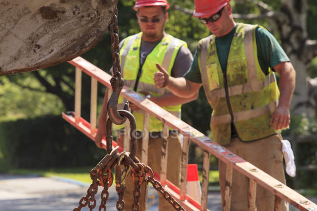 Trabajadores de la construcción señalando la cadena de elevación del operador de la excavadora - foto de stock