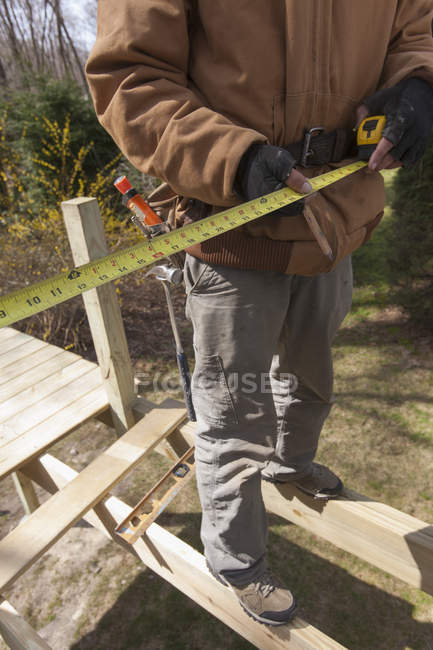 Carpintero de pie en vigas de cubierta haciendo la medición de cinta - foto de stock