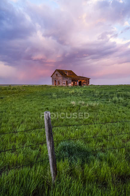 Abandoned barn on farmland with storm clouds glowing pink; Val Marie, Saskatchewan, Canada — Stock Photo