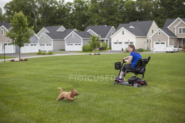 Giovane donna con paralisi cerebrale cavalcando il suo scooter sul suo prato — Foto stock