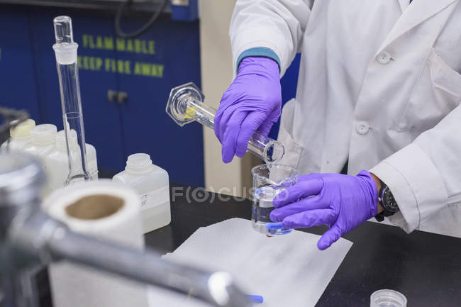 Técnico de laboratorio agregando líquido del cilindro graduado al vaso de precipitados - foto de stock
