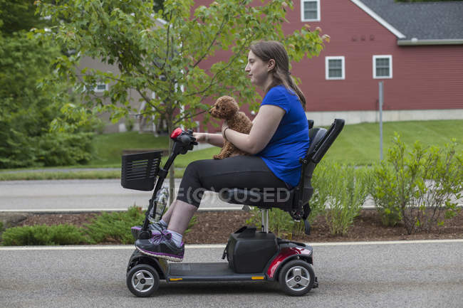 Mujer joven con parálisis cerebral montando el scooter con su perro - foto de stock