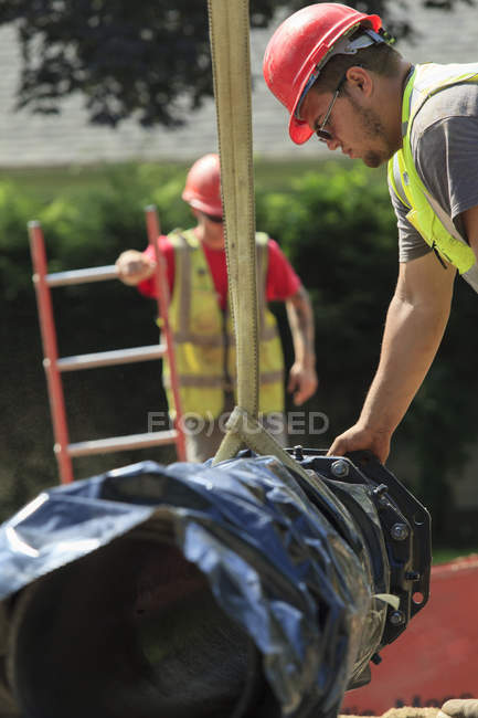 Construction worker using strap on excavator to guide water main section — Stock Photo