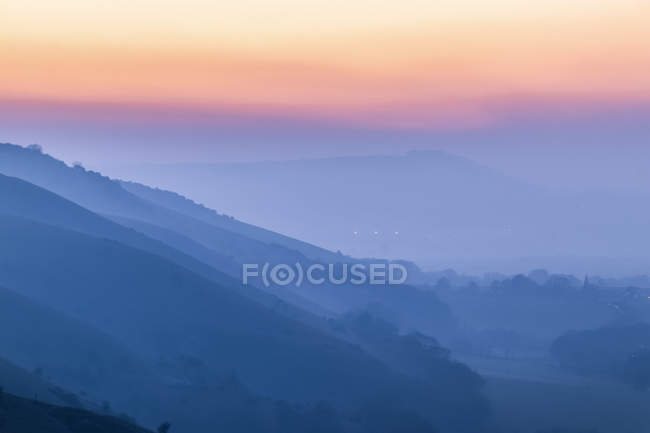 Couches silhouettées de collines et un coucher de soleil coloré à travers le brouillard dans le parc national South Downs ; Brighton, Sussex Est, Angleterre — Photo de stock