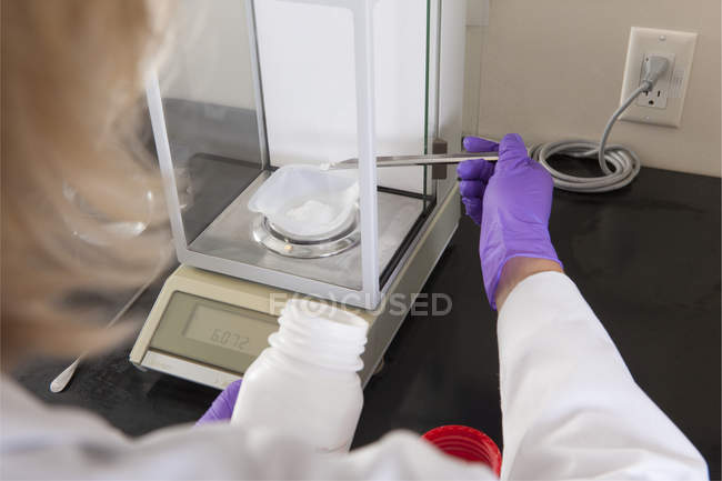 Científico de laboratorio agregando una pequeña cantidad de reactivo sólido a un contenedor a una escala - foto de stock