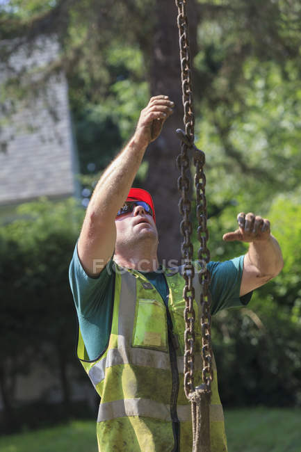 Construction worker guiding chain attached to excavator — Stock Photo