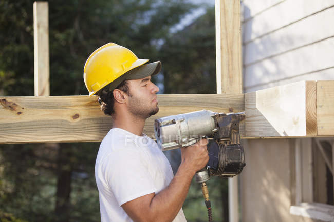 Hispanic carpenter using nail gun on home deck construction — Stock Photo