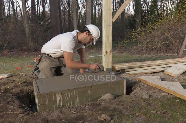 Hispanic carpenter putting smooth edge on stairway footing concrete — Stock Photo