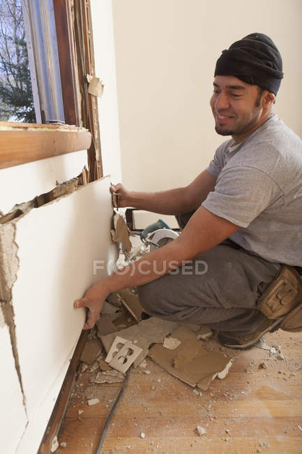 Hispanic carpenter removing cut wallboard under house window — Stock Photo