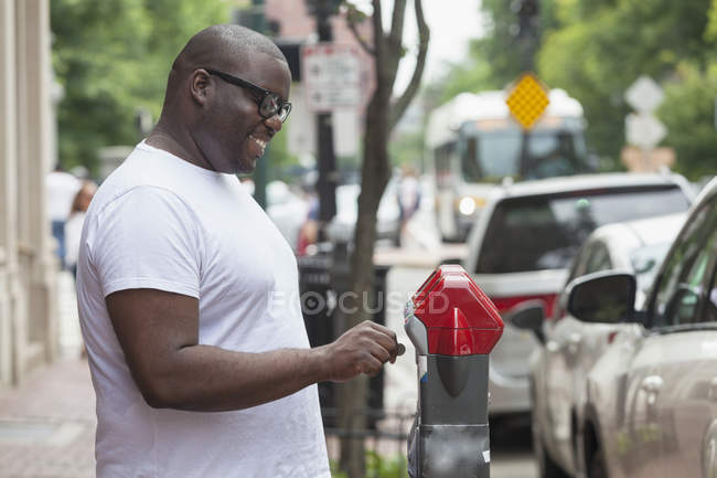 Hombre con TDAH insertando moneda en un parquímetro en la calle de la ciudad - foto de stock