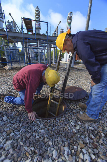 Power engineers placing ladder inside manhole at high voltage power distribution station — Stock Photo