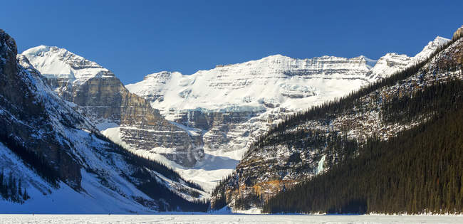 Panorama view of snow-covered glacier mountain, snow-covered lake with deep blue sky; Lake Louise, Alberta, Canada — Stock Photo