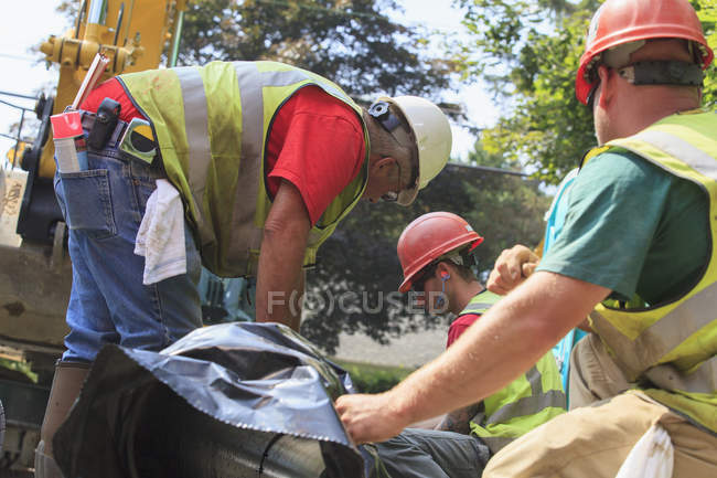 Construction workers preparing for excavator to lift water main into place — Stock Photo