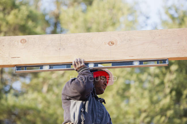 Carpintero midiendo viga horizontal del techo - foto de stock