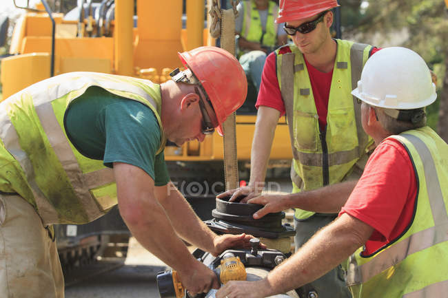 Trabajadores de la construcción que utilizan una llave accionada por batería para asegurar la sección principal de agua con pernos - foto de stock